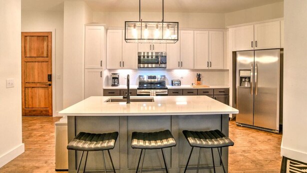 A modern kitchen with white cabinets, stainless steel appliances, a large island with bar stools, and pendant lighting.