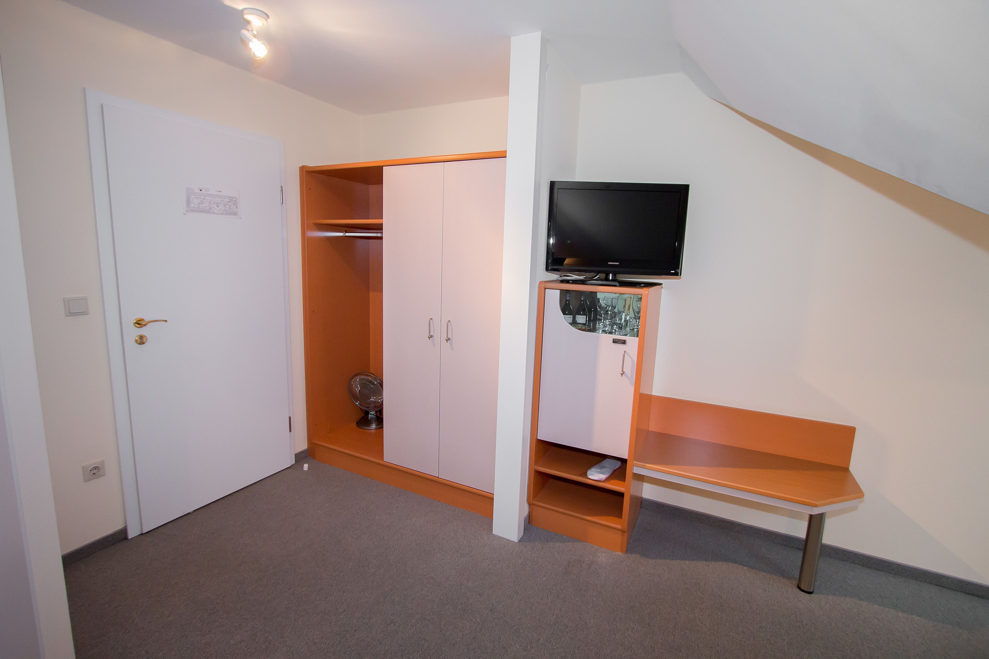 A room with a white door, a wardrobe, a television on a stand, and a small wooden bench.