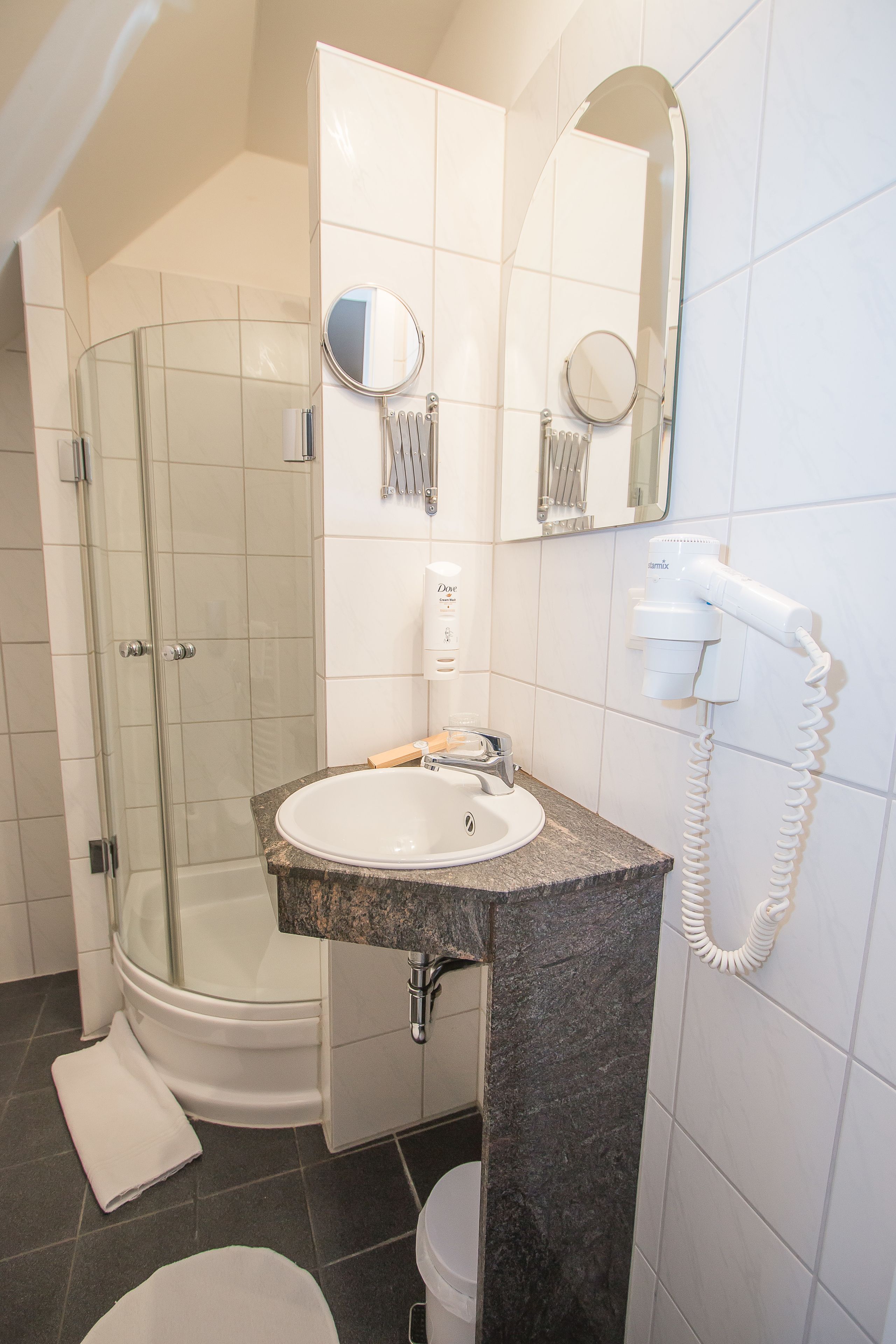 Une salle de bain dotée d’une douche à parois de verre, d’un lavabo avec un plan de toilette en marbre et d’un sèche-cheveux fixé au mur.