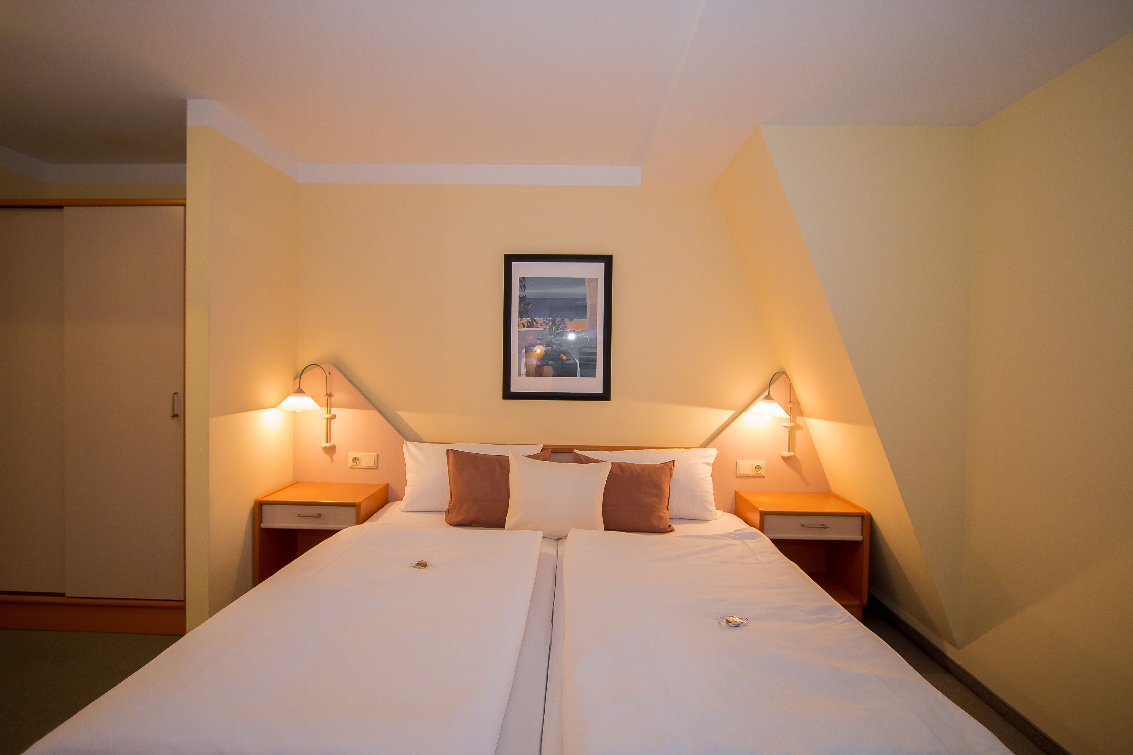 Una cama doble con dos mesitas de noche, cada una con una lámpara, en una habitación con un cuadro en la pared.