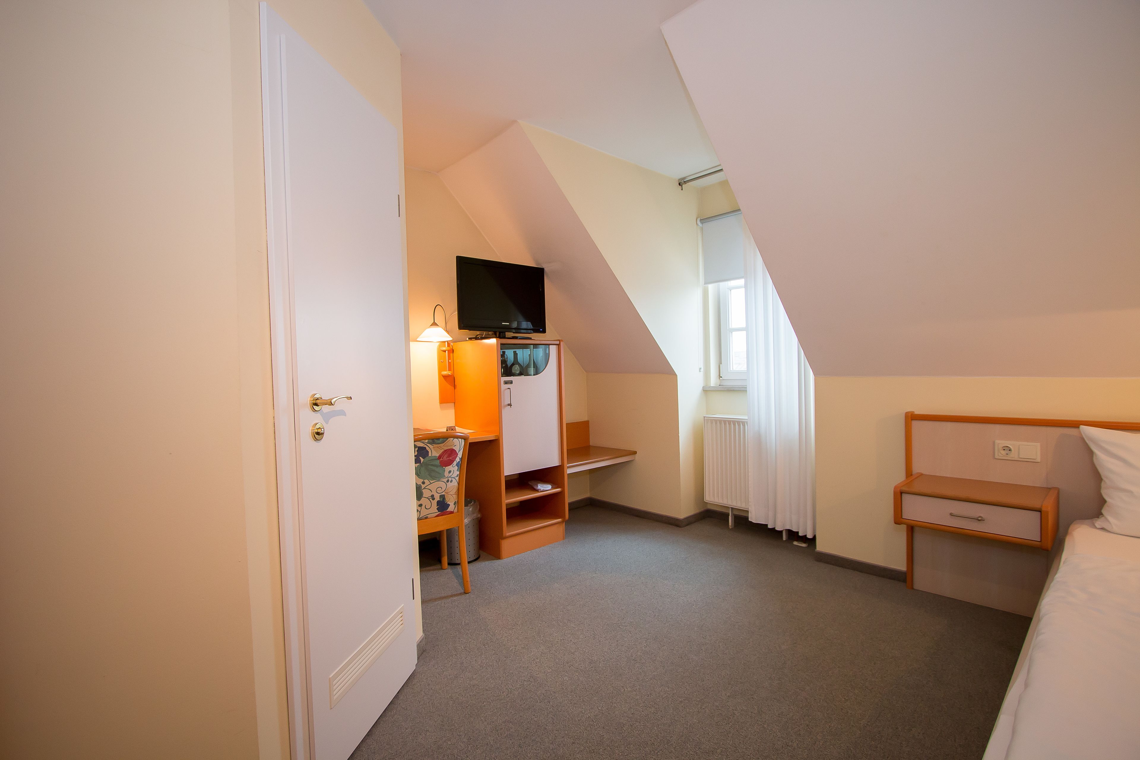 Een slaapkamer met een bed, een bureau met stoel, een televisie op een meubel en een radiator.