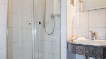 Een douche met glazen wanden, een wit wastafelmeubel en een spiegel.