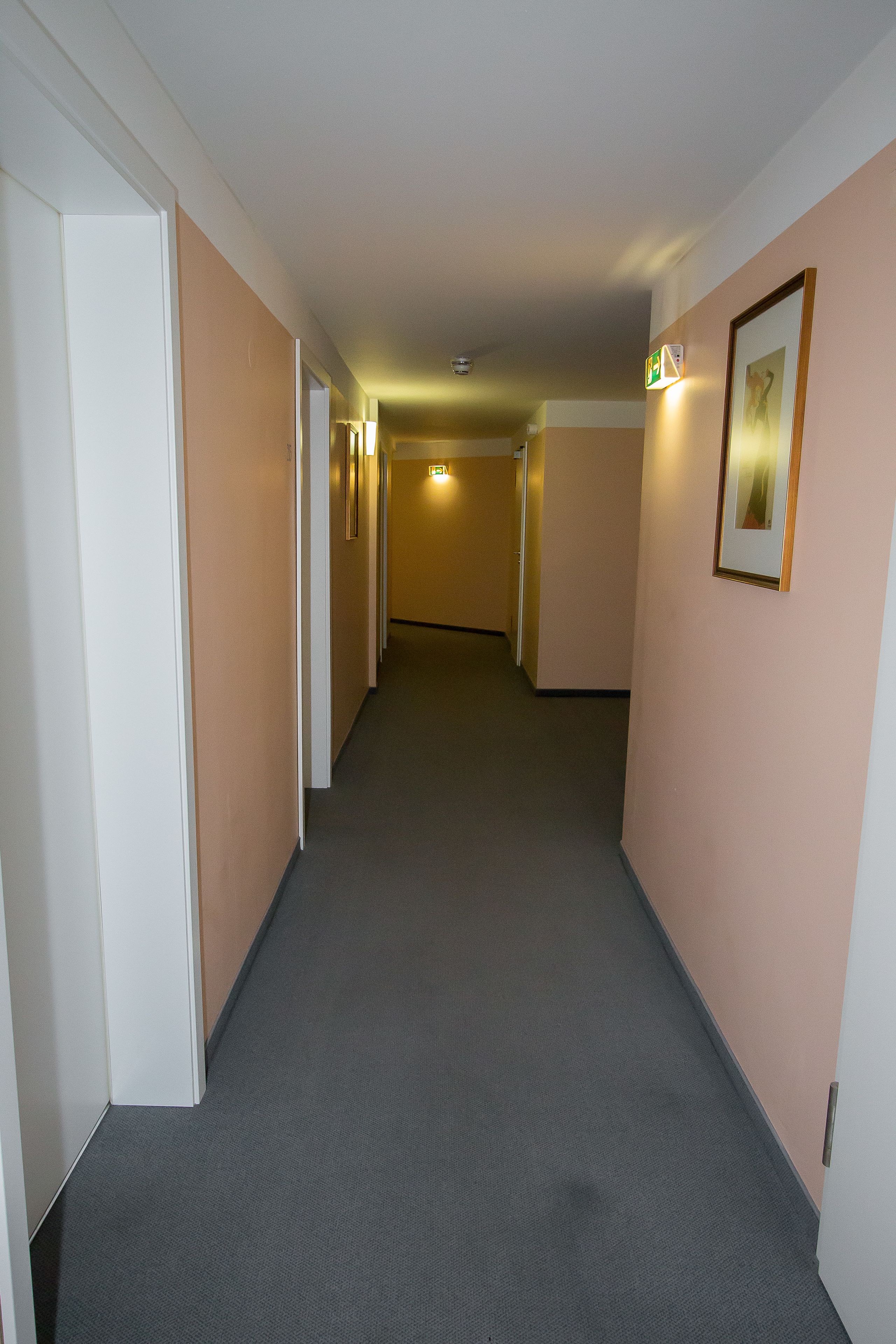 A corridor with beige walls, a grey carpet, and framed pictures on the right.