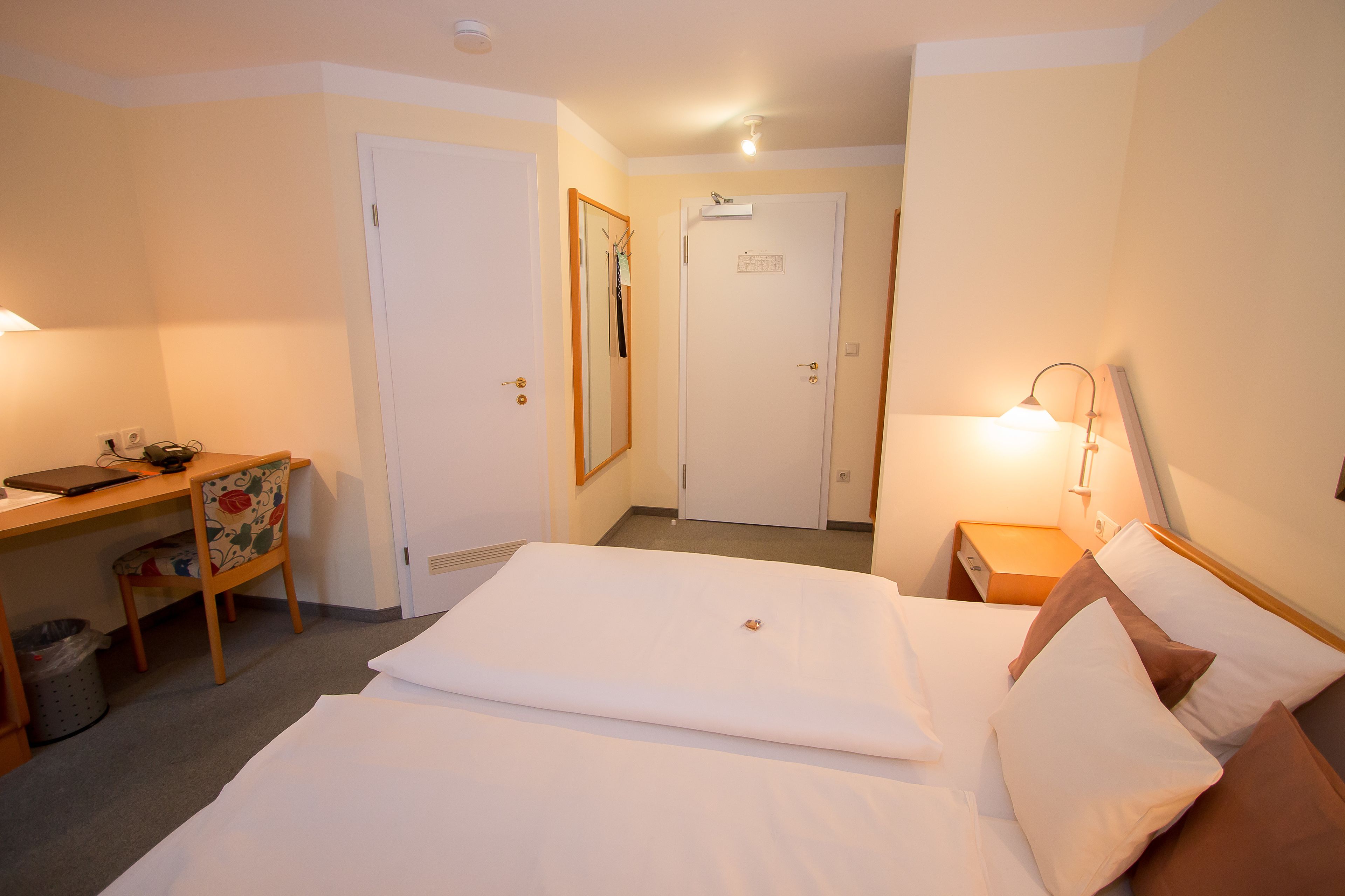 Ein Hotelzimmer mit Bett, Schreibtisch, Stuhl und Nachttisch mit Lampe.