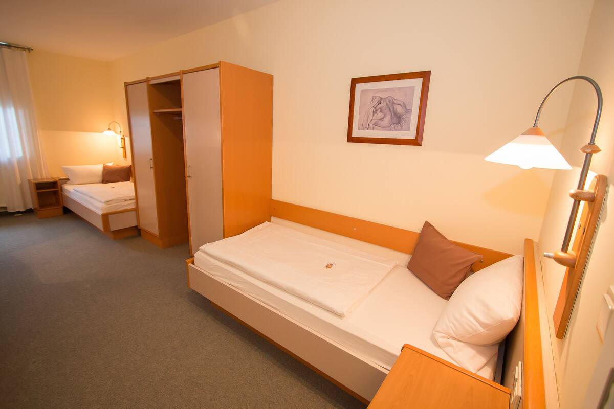 Una habitación de hotel con una cama individual, una mesita de noche, un armario y un cuadro en la pared.