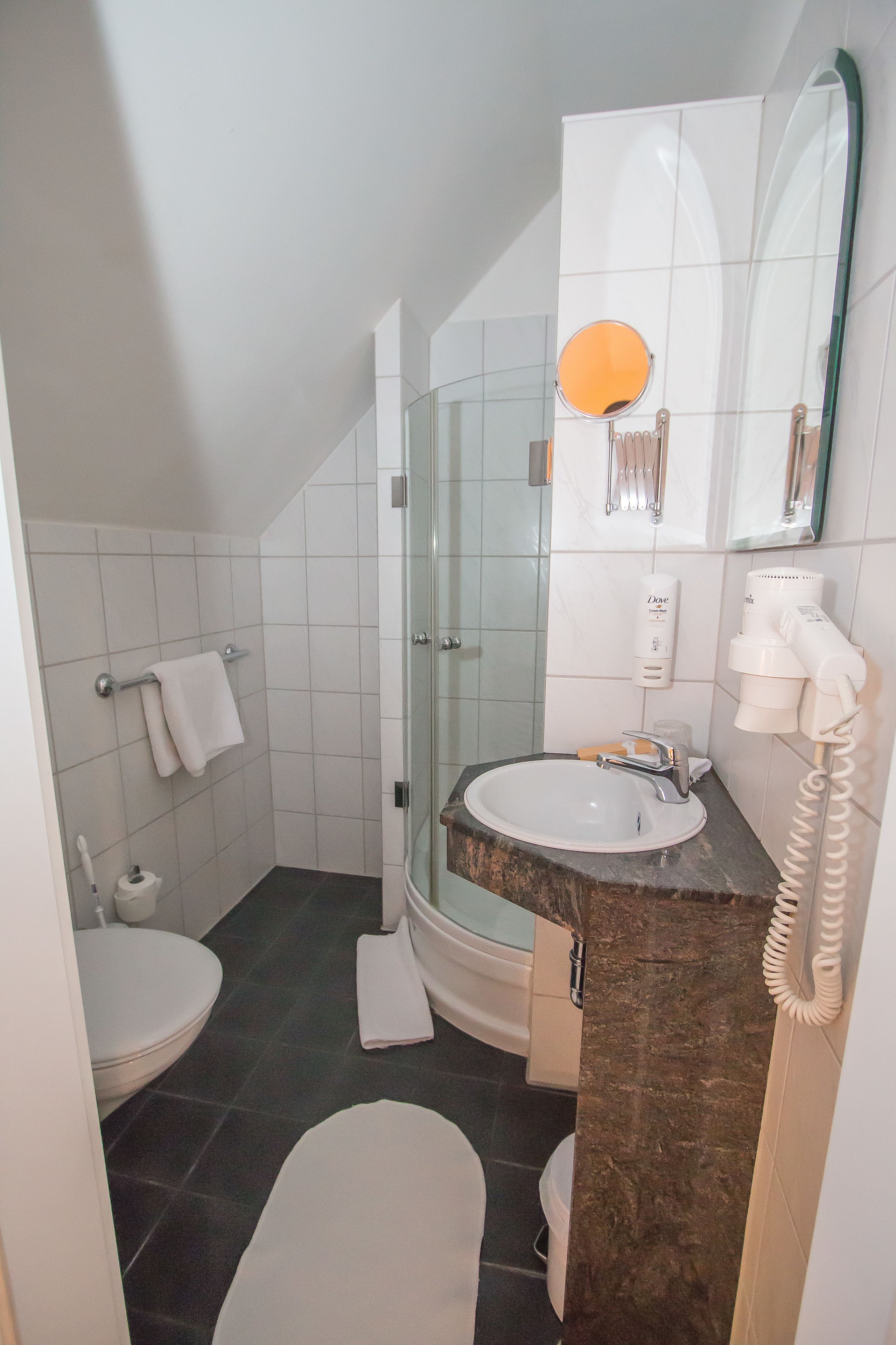 A bathroom with a glass shower enclosure, a sink with a marble countertop, a toilet, and a towel rack.
