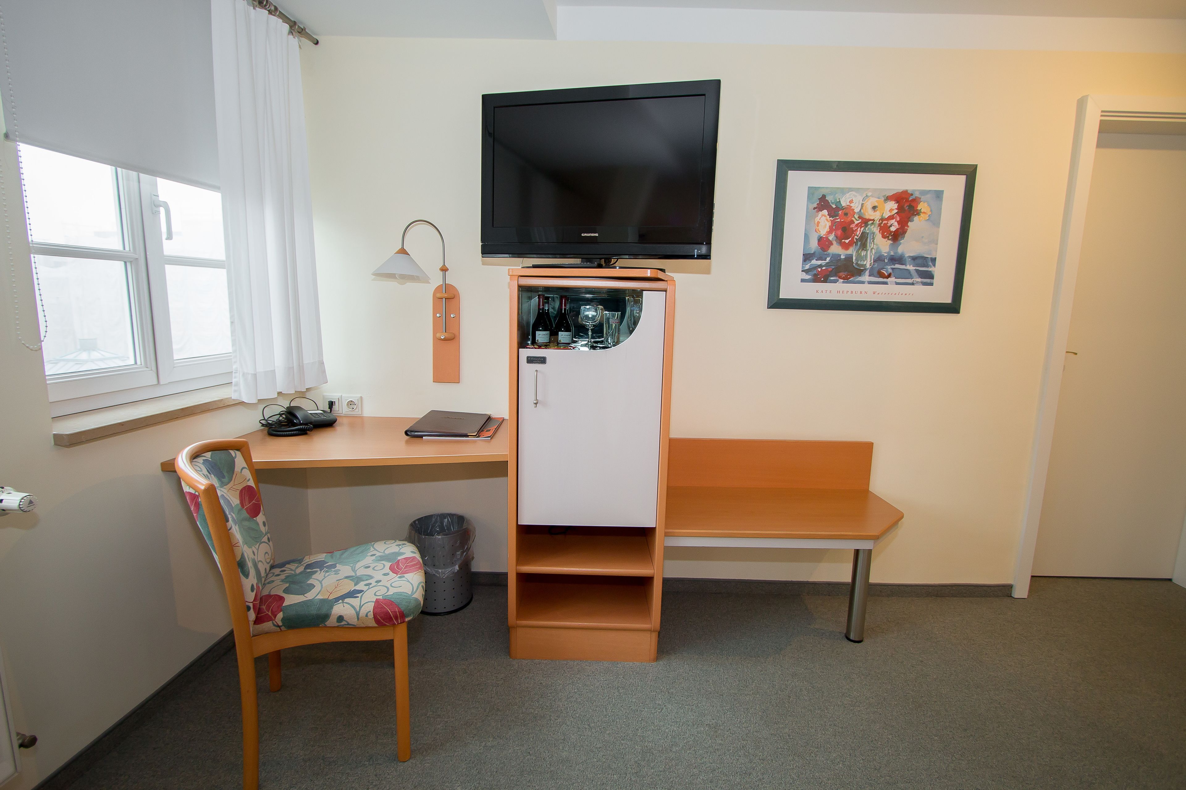 A compact room with a desk, chair, TV, and a small fridge.