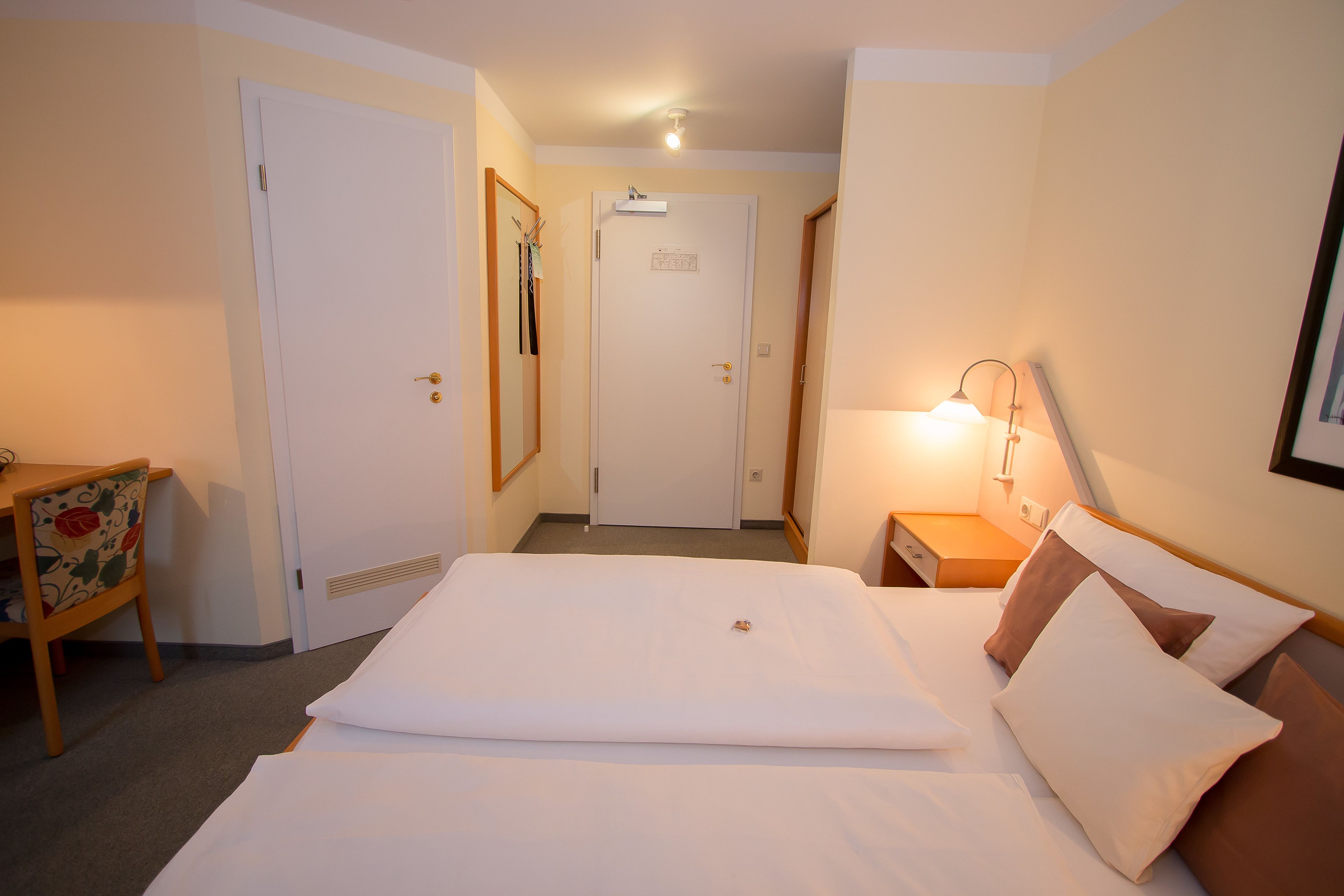 Una habitación de hotel con una cama, un escritorio, una silla, una lámpara y una puerta.