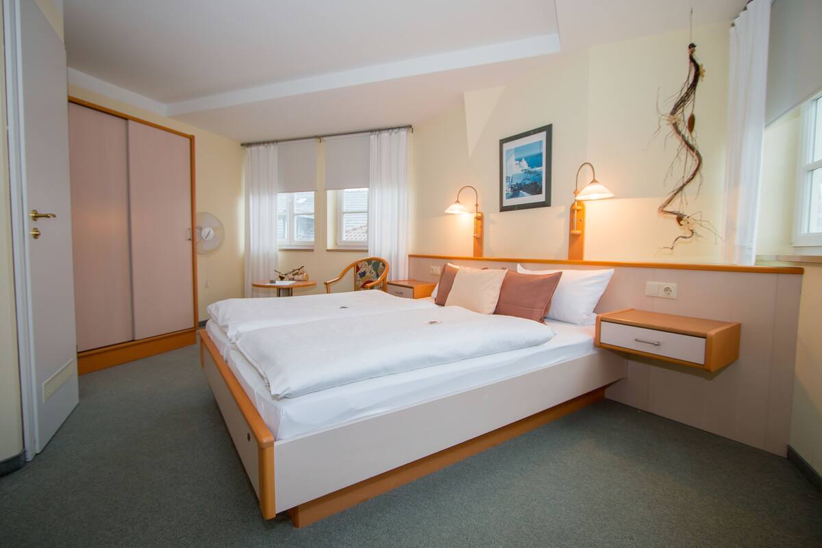 Un dormitorio con cama, mesitas de noche, un sillón, escritorio y armario.