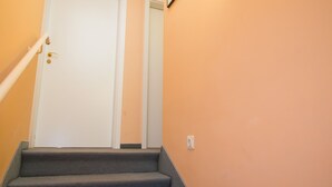 Una escalera con peldaños alfombrados que conduce a una puerta blanca, una lámpara empotrada en la pared y un cuadro enmarcado.