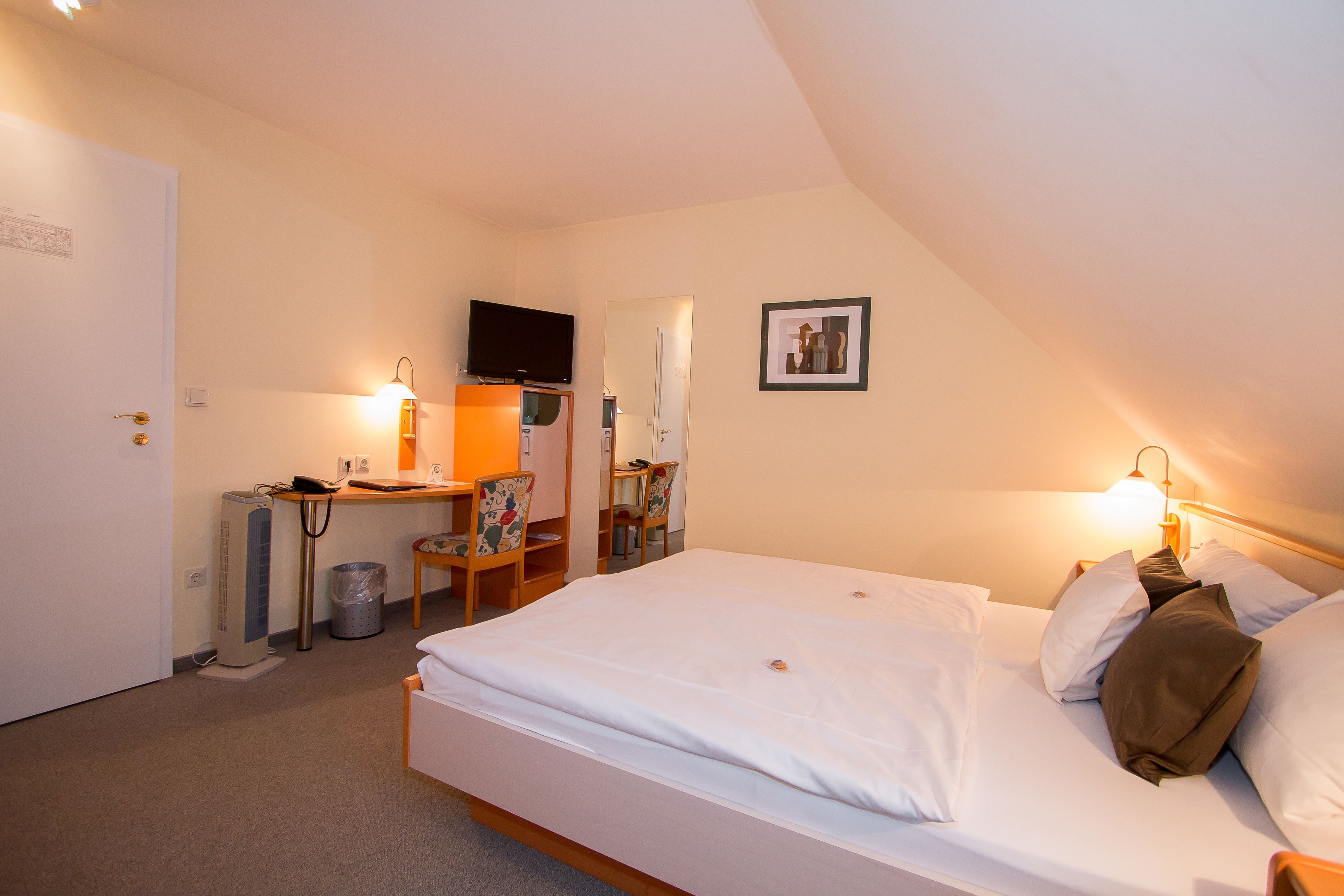 Habitación de hotel con cama, escritorio, silla, televisor y un cuadro en la pared.