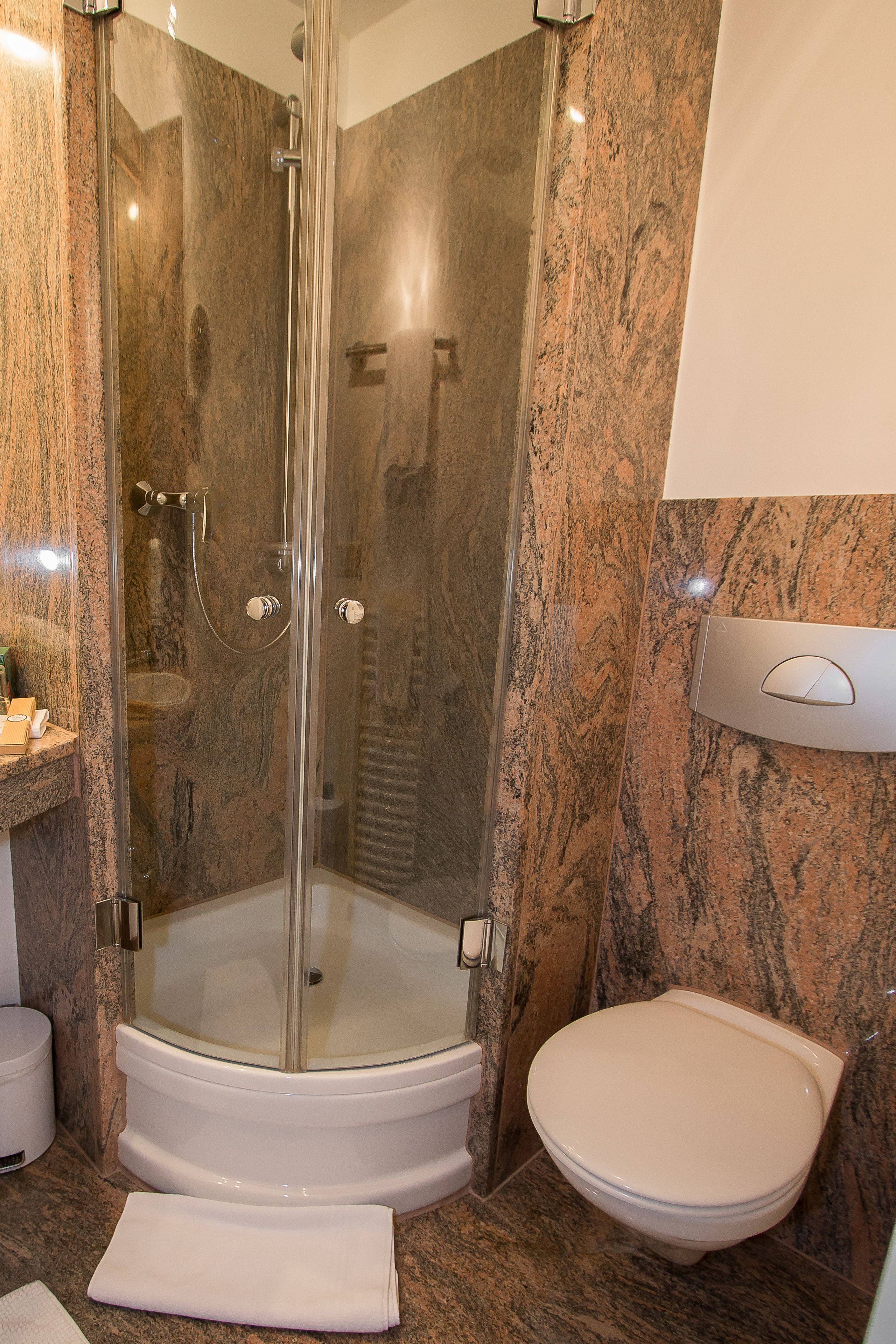 Een badkamer met een douchecabine van glas, een wit toilet en een wand betegeld met marmer.