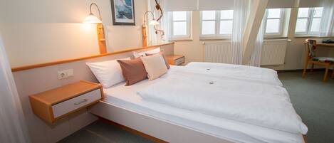 A hotel room with a large bed, bedside tables, a chair, and a window with curtains.