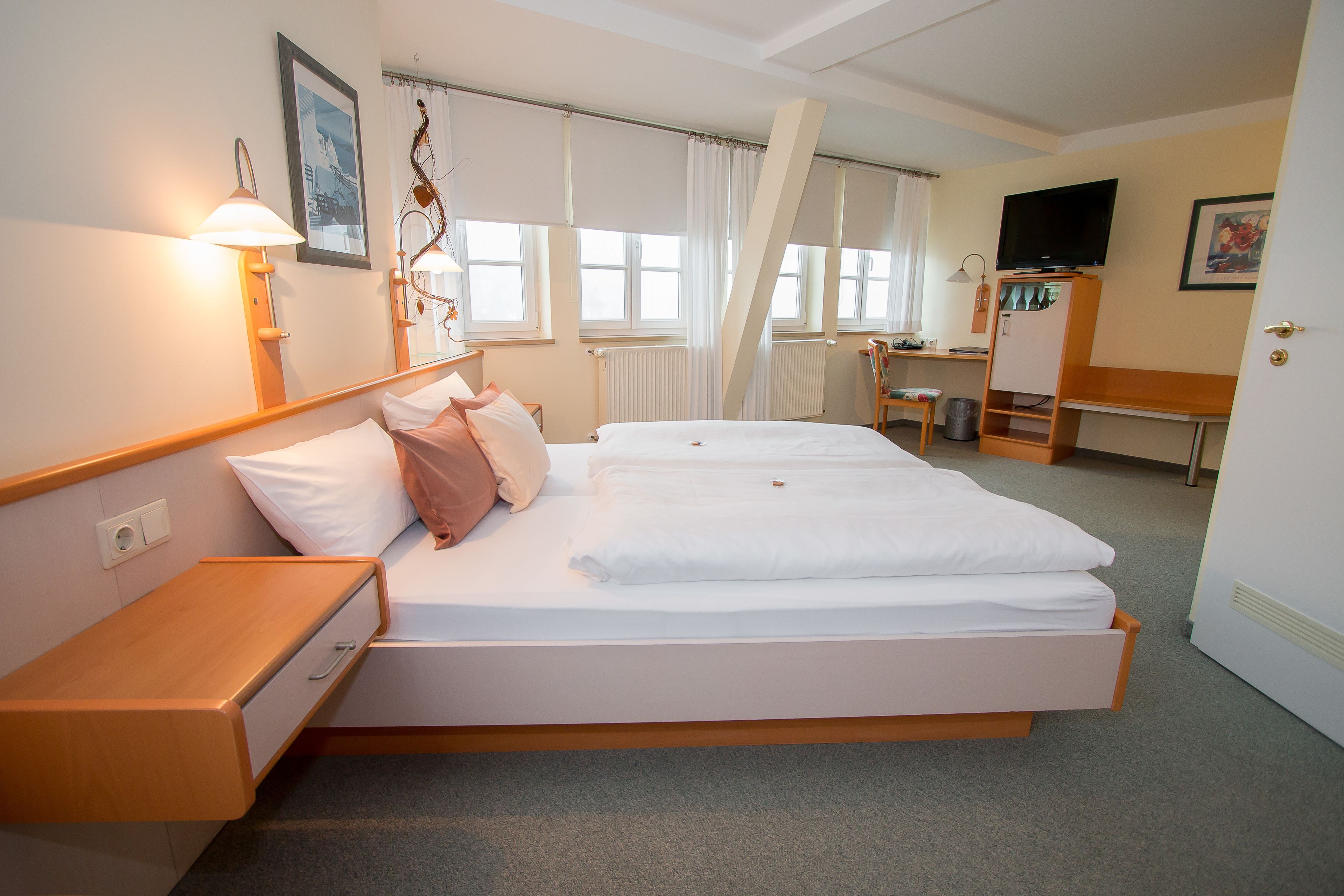 A hotel room with a double bed, a desk with a chair, a television, and a radiator.
