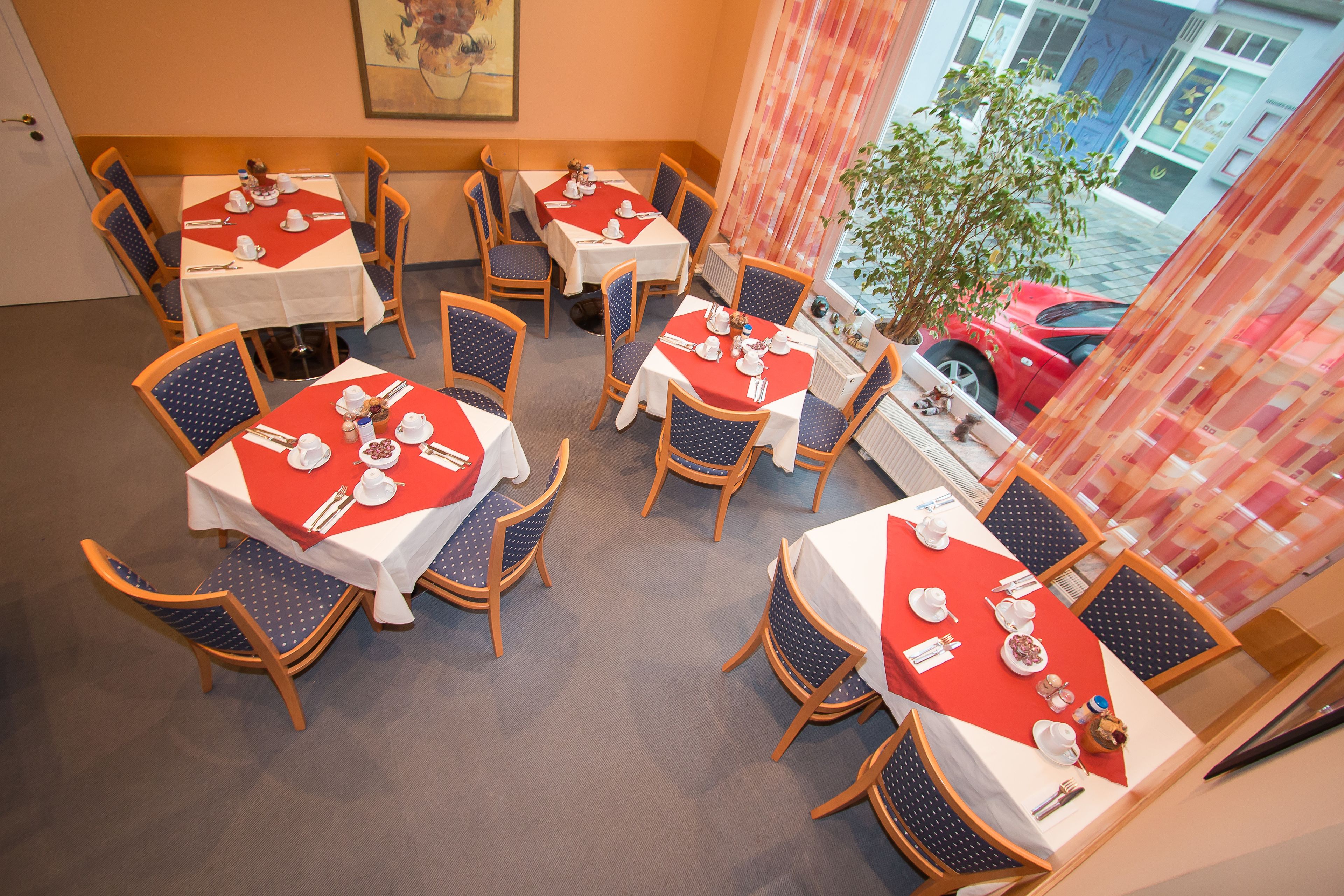A dining area with multiple tables set for meals, chairs, and a view of the street outside.
