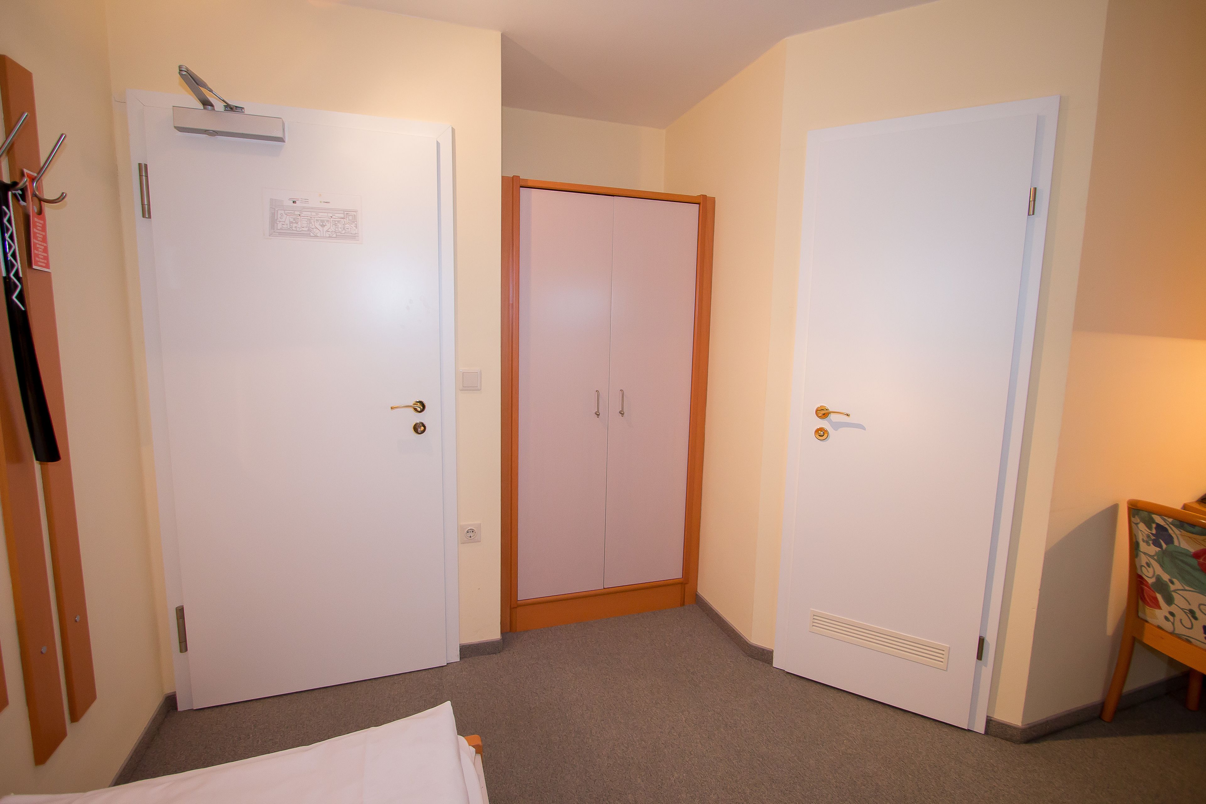Habitación de hotel con dos puertas blancas, un armario de madera y una mesita con un cuadro de colores.