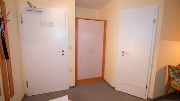 Habitación de hotel con dos puertas blancas, un armario de madera y una mesita con un cuadro de colores.