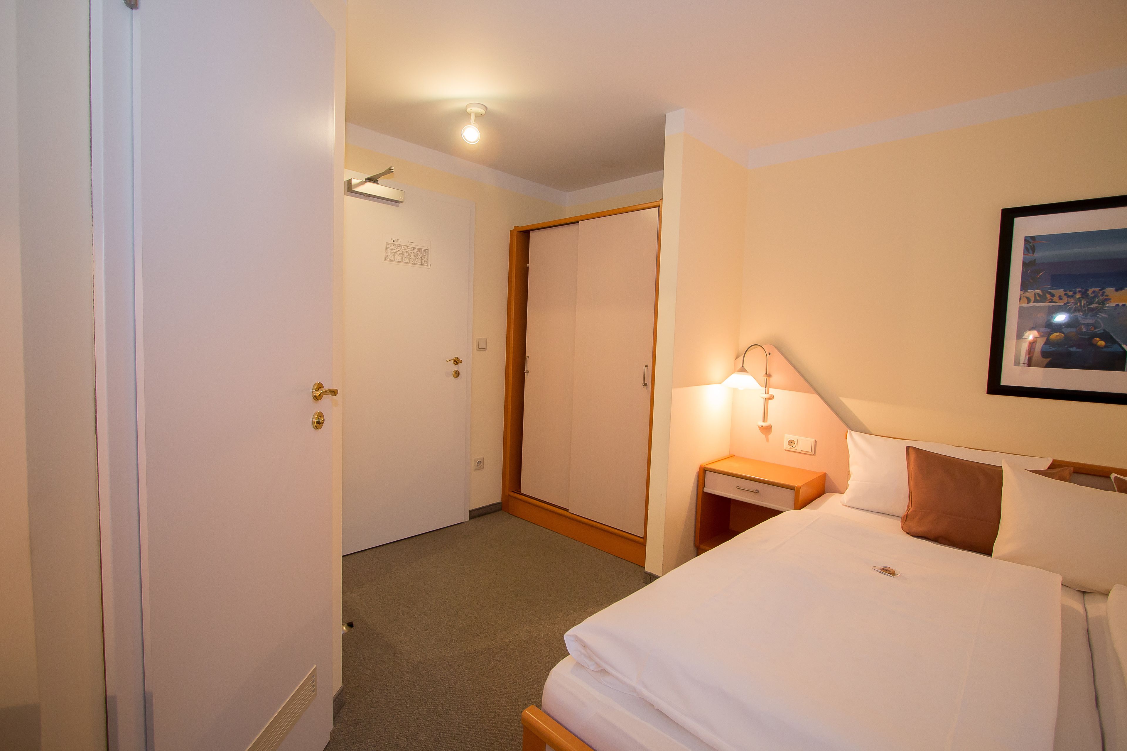 Une chambre d’hôtel avec un lit, une table de chevet, une lampe et une armoire.