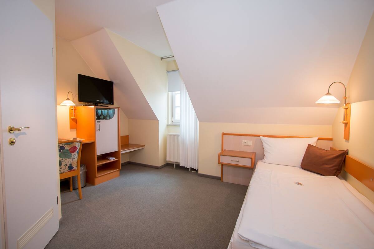 Una habitación de hotel con cama, escritorio, silla, televisor y ventana.