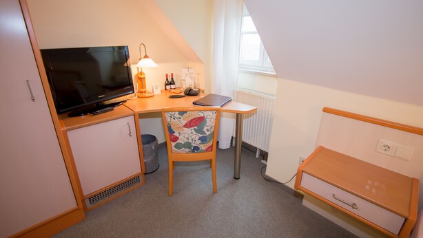 Una habitación pequeña y acogedora con escritorio, silla, televisor y radiador.