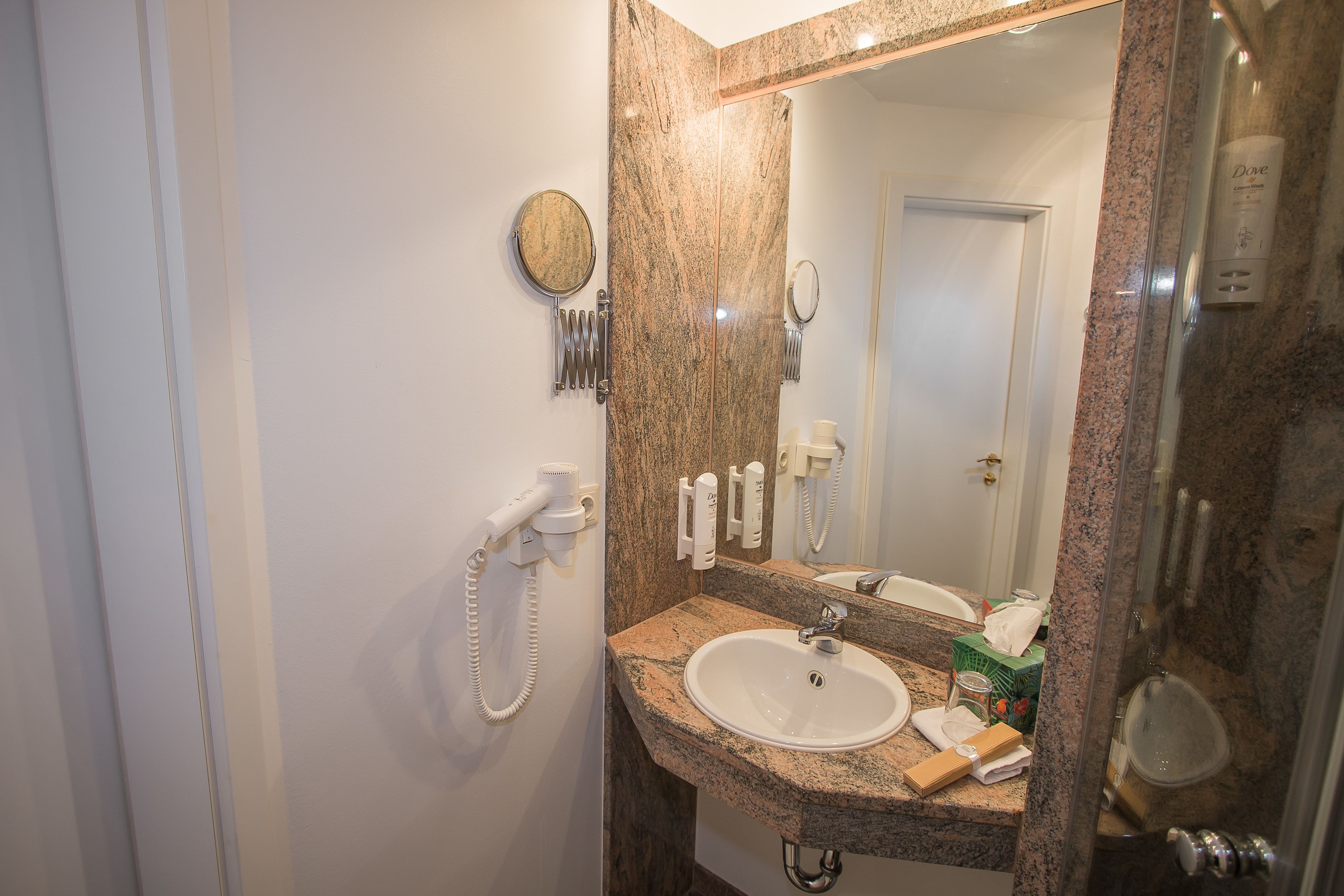 Un baño con encimera de granito, lavabo, espejo, secador de pelo y artículos de aseo.