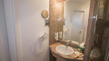Un baño con encimera de granito, lavabo, espejo, secador de pelo y artículos de aseo.