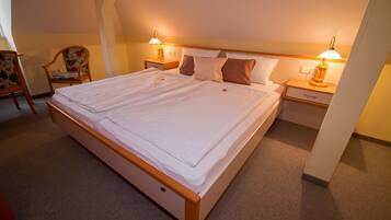 A double bed with a wooden frame, two bedside tables with lamps, a chair with a floral pattern, and a carpeted floor.