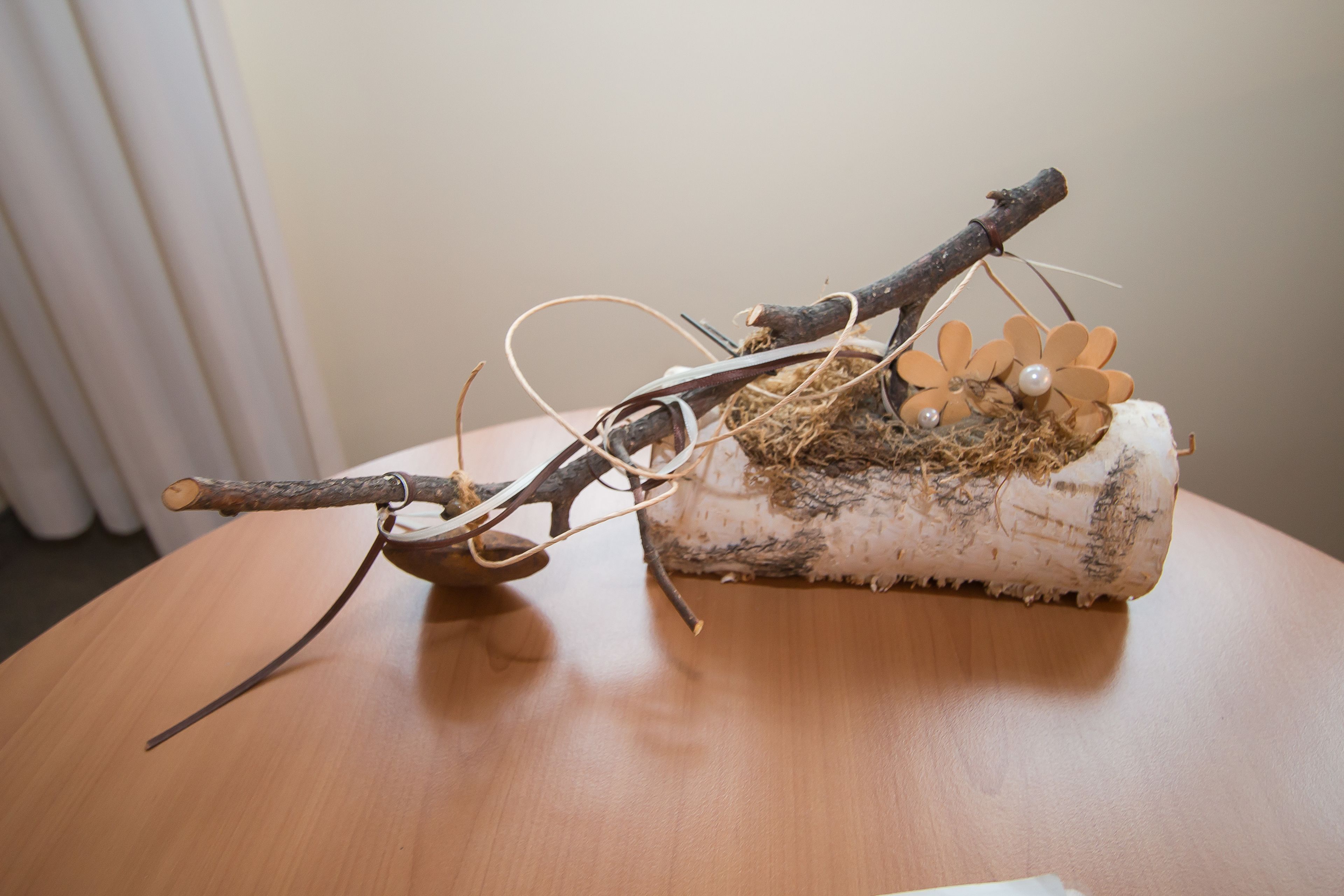 A wooden table with a decorative branch and a nest-like structure containing a small bird figurine and a pearl.