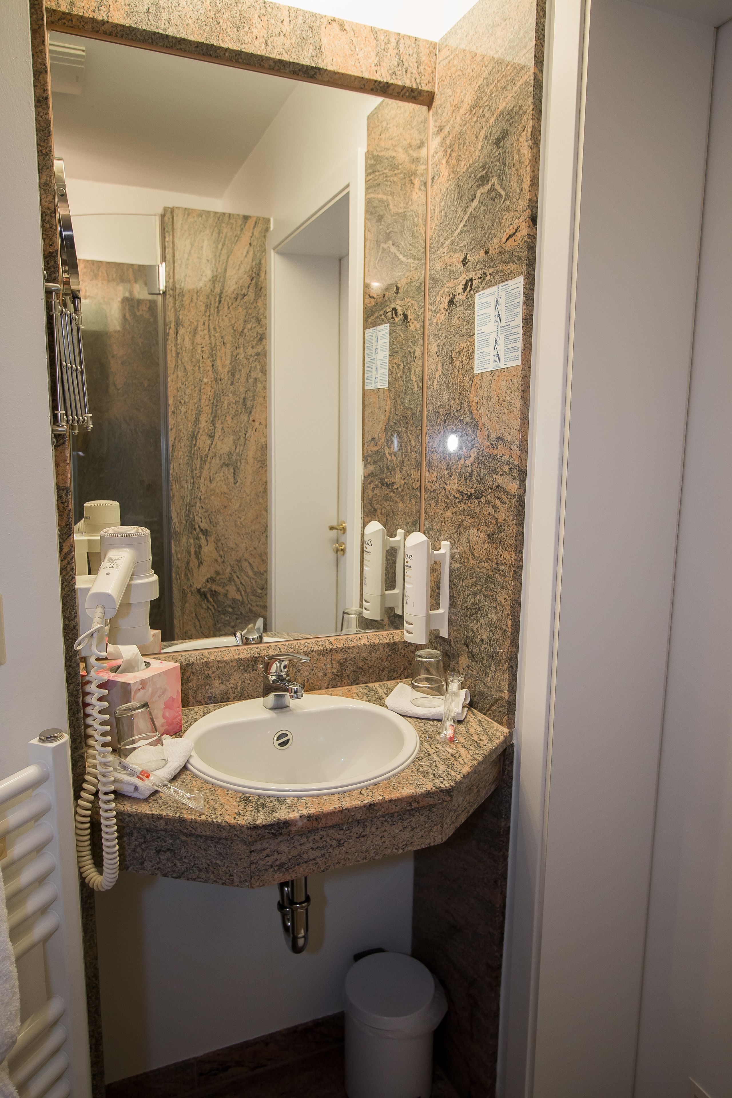 A bathroom with a granite countertop sink, a mirror, a towel rack, and a trash can.