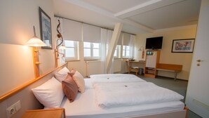 Habitación de hotel con dos camas, un escritorio, un televisor y una ventana con cortinas.