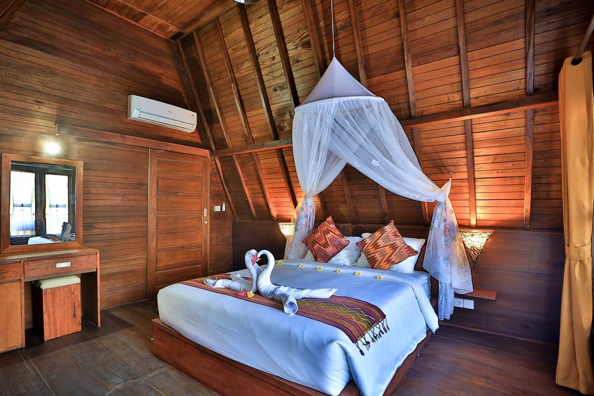 A wooden room with a bed, a vanity, and a mirror.