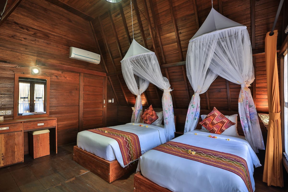 A wooden cabin bedroom with two beds, a desk, and an air conditioning unit.