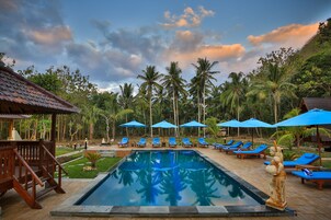 A pool area with lounge chairs and umbrellas, surrounded by palm trees and a wooden structure.