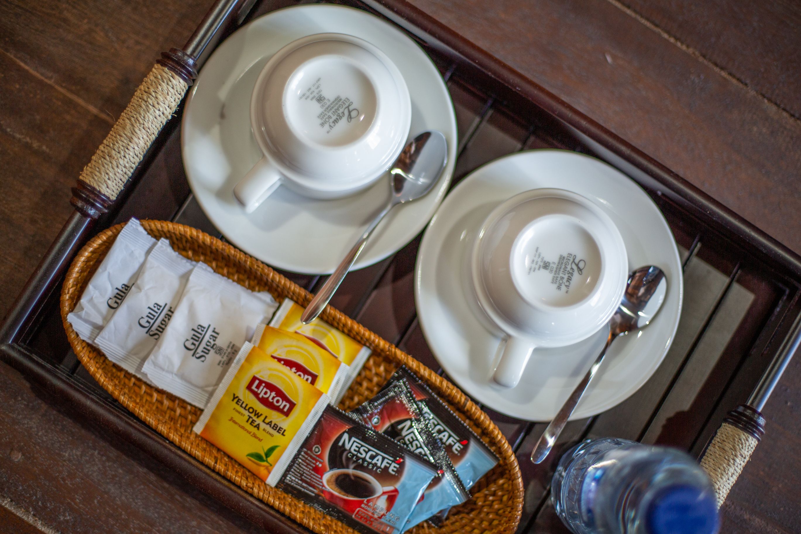Una bandeja con dos tazas y platillos blancos, una cuchara y una cesta que contiene sobrecitos de azúcar, té Lipton y café Nescafé.