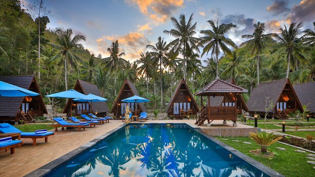 A resort with a swimming pool surrounded by lounge chairs and wooden huts with blue umbrellas. - Mahaloka Valley (Penida Island)