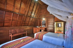 Una habitación de madera con techo inclinado, un banco de madera, dos camas con colchas estampadas, un aparador de madera, un espejo y un lavabo.