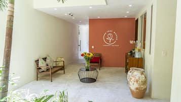 A hallway with a reception desk, a large vase with flowers, and a bench with cushions.