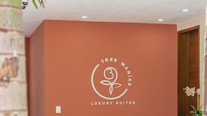 A reception area with a logo for 'Tres Marías Luxury Suites', a red wall, a wooden bench, a vase with flowers, and a plant in the foreground. - Tres Marias Luxury Suites - Adults Only (Puerto Vallarta)
