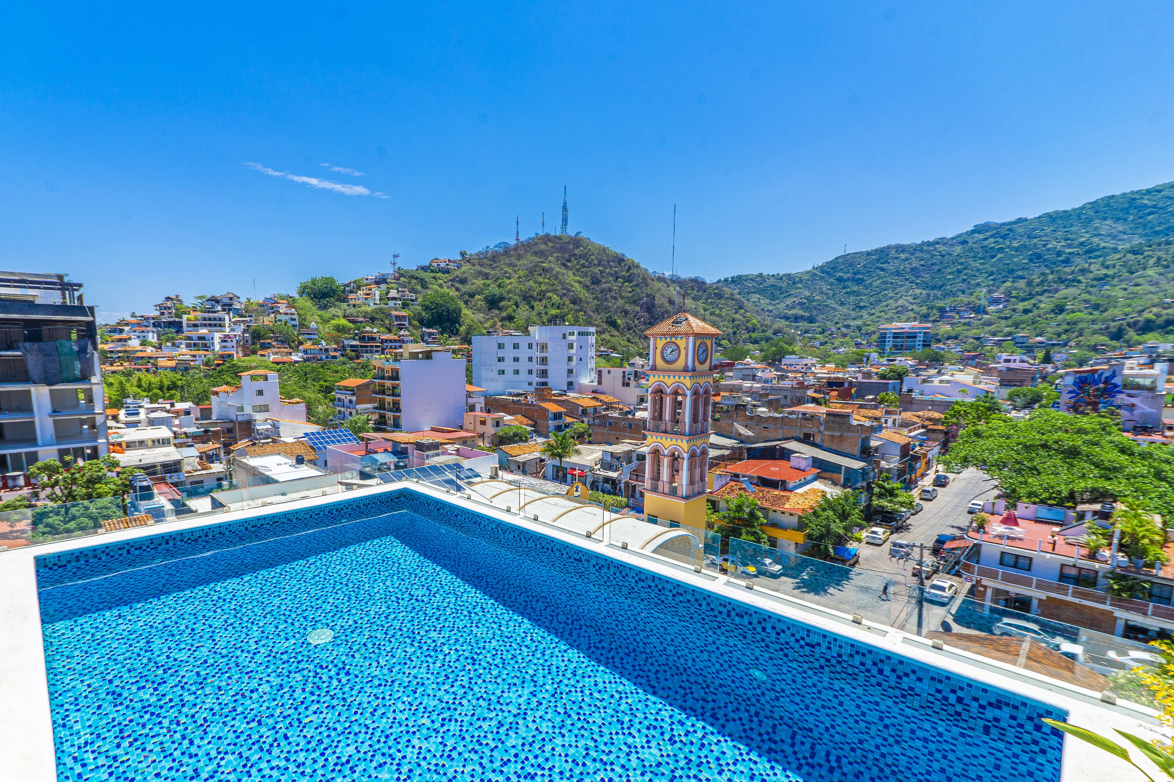 A swimming pool with a tiled deck, surrounded by buildings and a clock tower.
