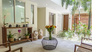 A lobby with a round black table, wooden benches, potted plants, and a large mirror. - Tres Marias Luxury Suites - Adults Only (Puerto Vallarta)