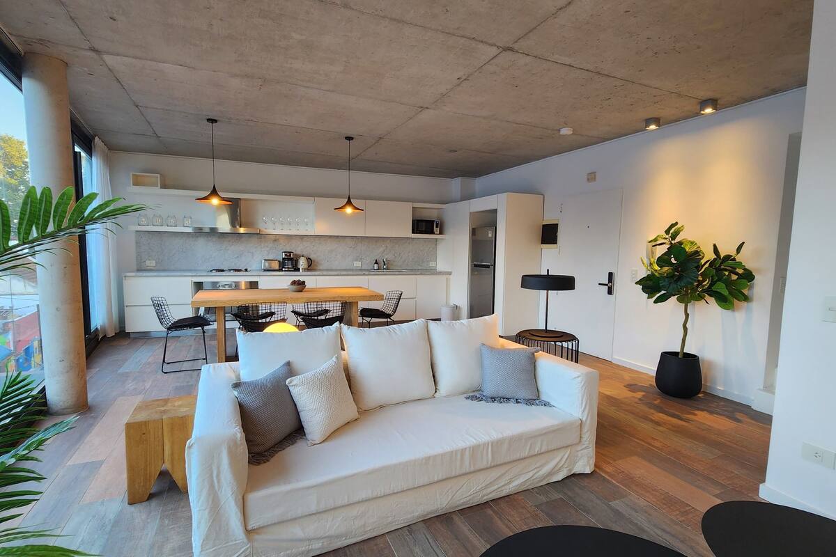 A modern living room with a sofa, a dining table, and a kitchen in the background.