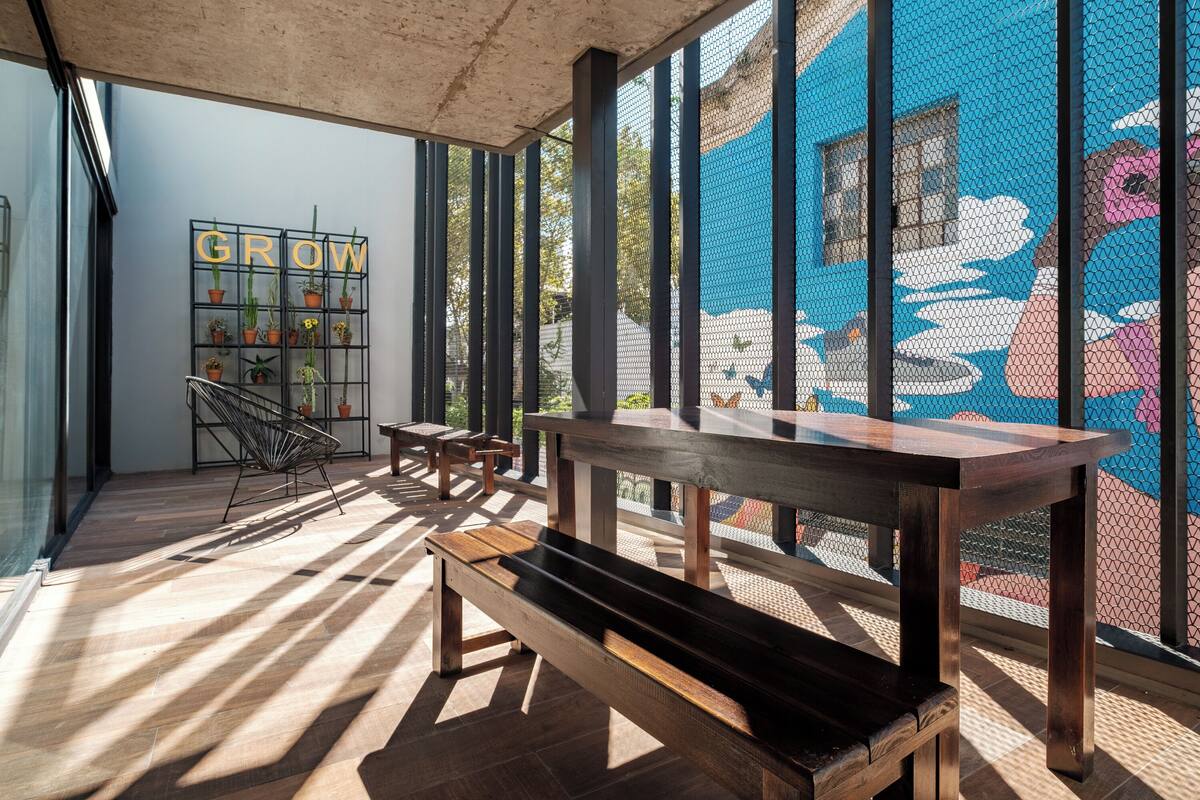 An indoor seating area with wooden benches and tables, a wall-mounted plant display, and a colorful mural.