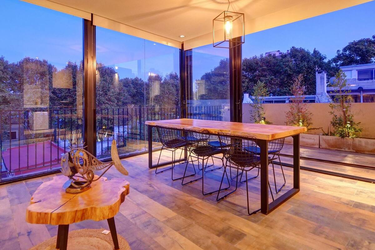 A modern dining area with a wooden table and chairs, large windows, and a view of the cityscape.