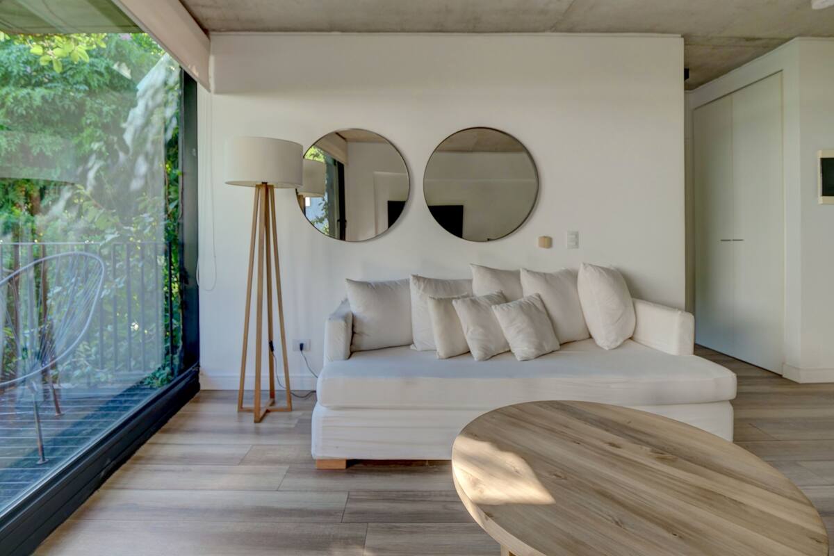 A modern living room with a white sofa, two round mirrors, a floor lamp, and a wooden coffee table.