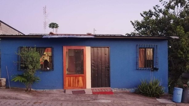 Ein kleines, eingeschossiges Gebäude mit blauer Fassade, einer Holztür und einer kleinen Veranda.