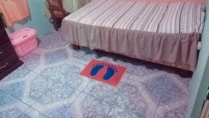 Ein Schlafzimmer mit Bett, Stuhl, kleinem Tisch und einer rosa Fußmatte.