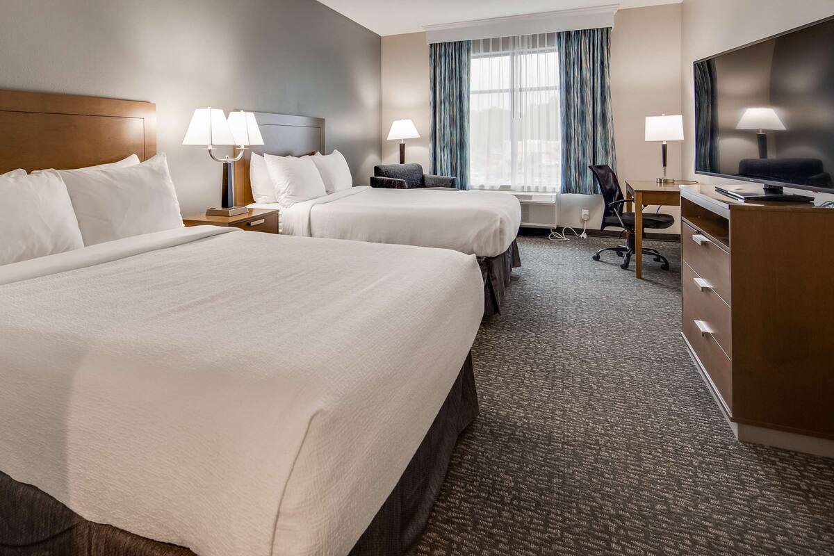 Hotelkamer met twee bedden, een bureau, een stoel, een televisie en een raam met gordijnen.