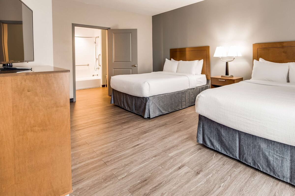 Een hotelkamer met twee bedden, een houten hoofdbord, een nachtkastje met een lamp en een houten vloer.