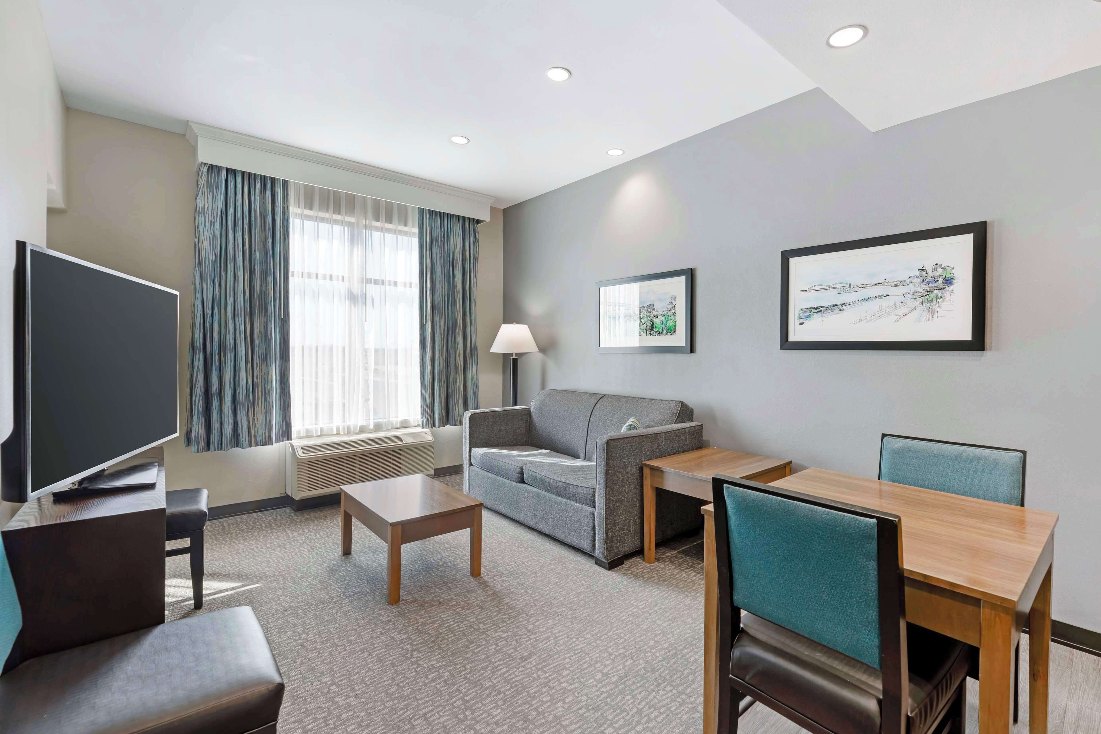 A hotel room with a flat-screen TV, a sofa, a table, and two chairs.