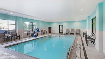 An indoor swimming pool with a tiled deck, lounge chairs, and a door leading to another room.